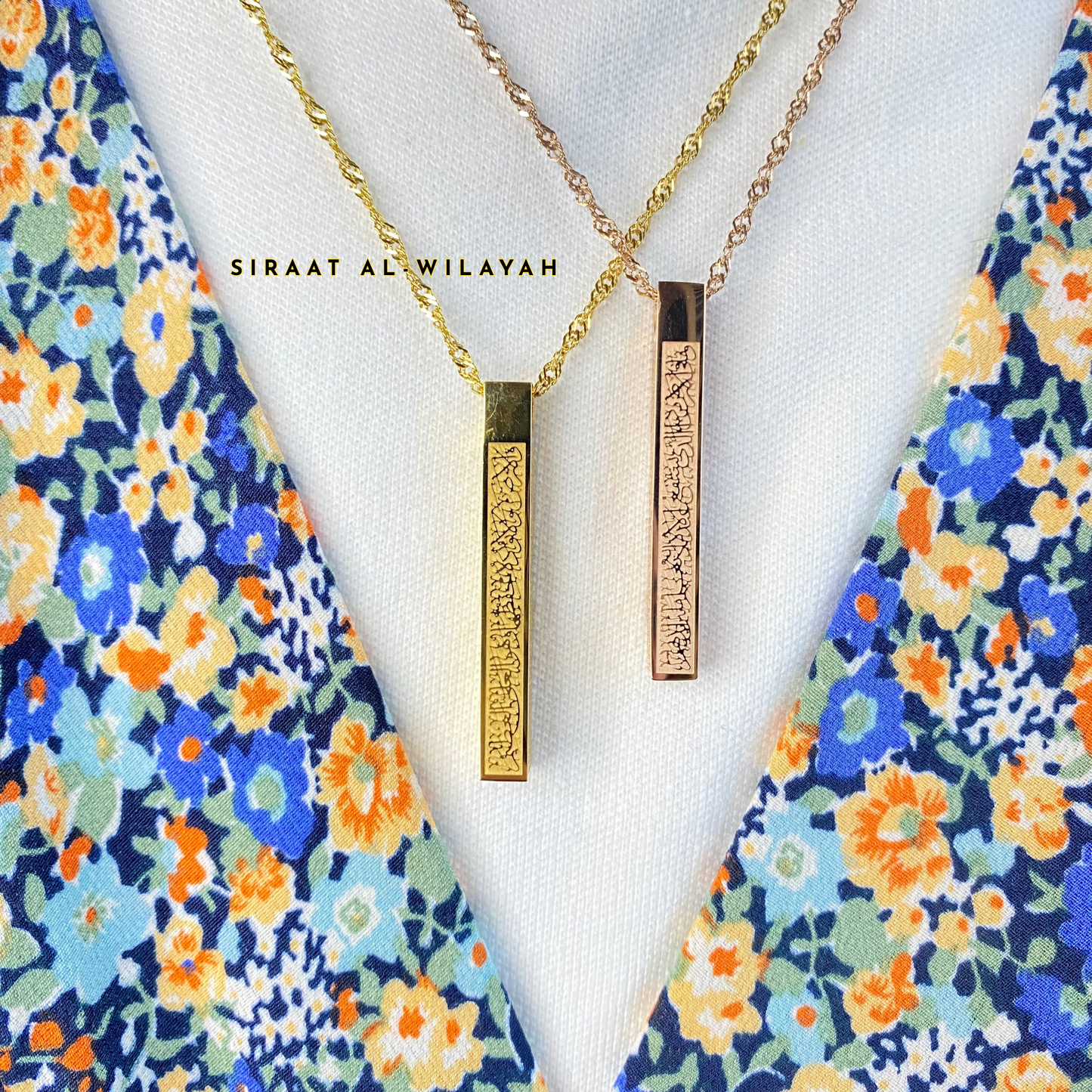 Two ayatul kursi necklaces with vertical pendants on a floral background, featuring the brand 'Siraat Al-Wilayah'.